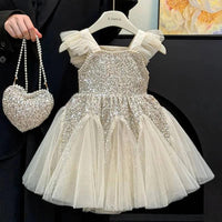 toddler girl ivory sequin party dress with tulle skirt and ruffled straps holding matching heart purse