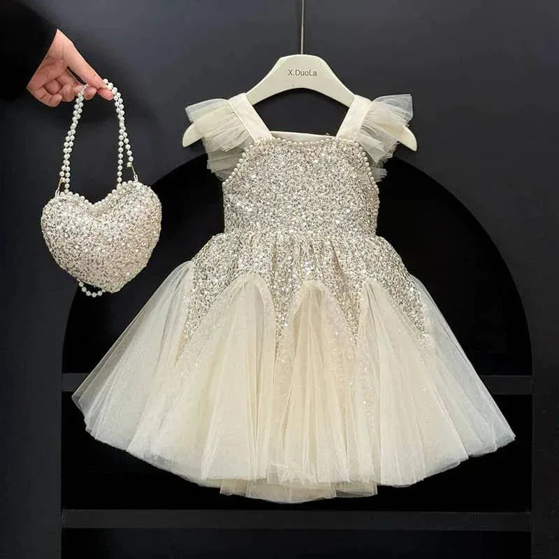 baby girl ivory sequin party dress with tulle skirt and ruffle straps hanging on hanger with matching heart-shaped sequin purse