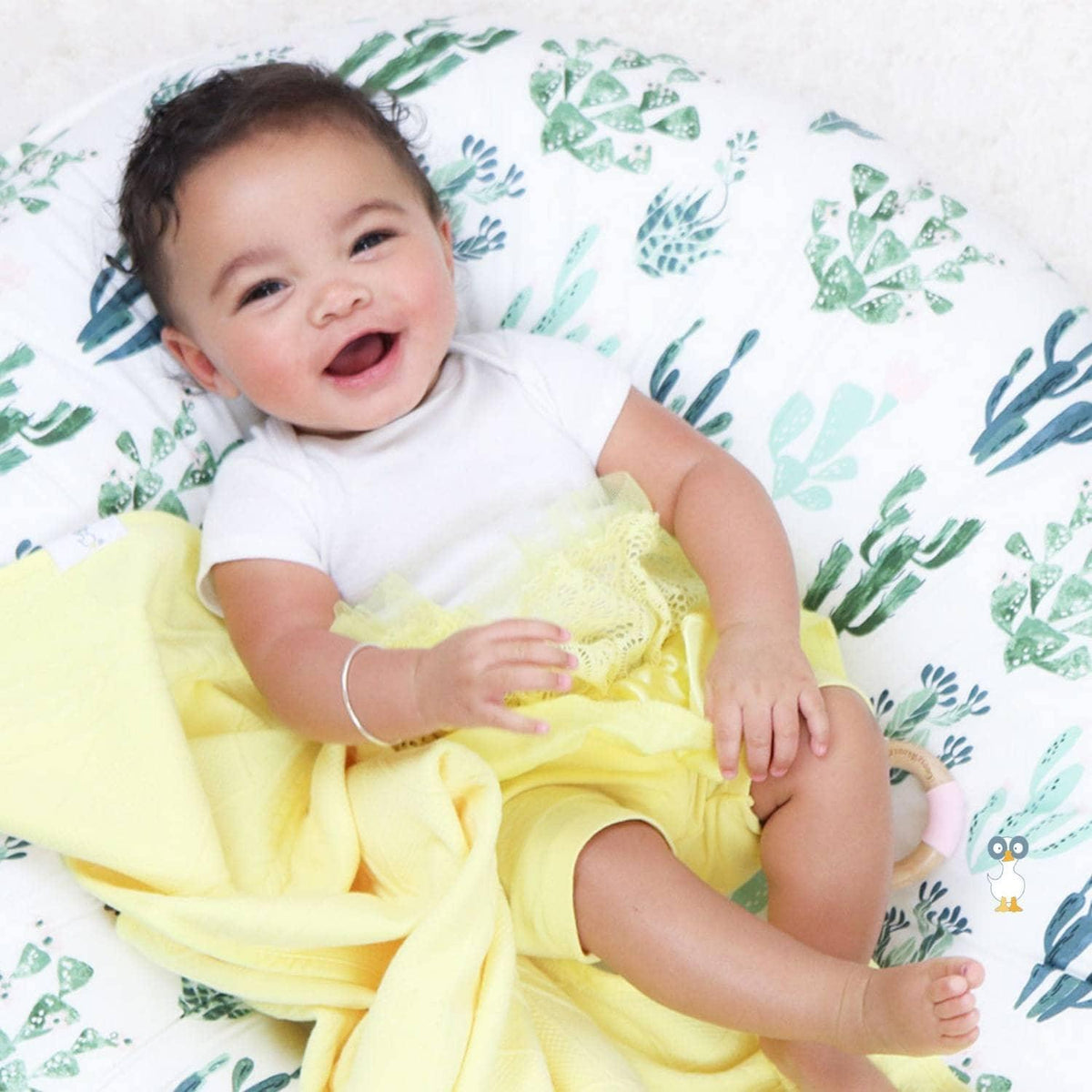 Smiling baby lying on green patterned cushion wrapped in yellow knit baby blanket