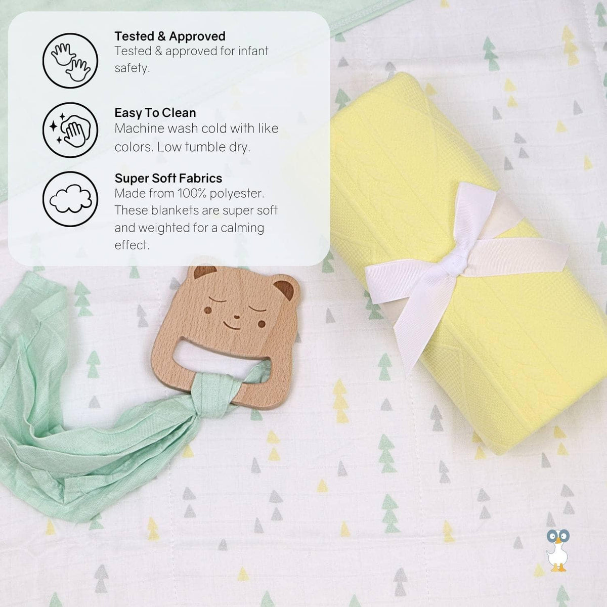 Rolled yellow knit baby blanket with white ribbon and wooden bear teether on a patterned baby sheet