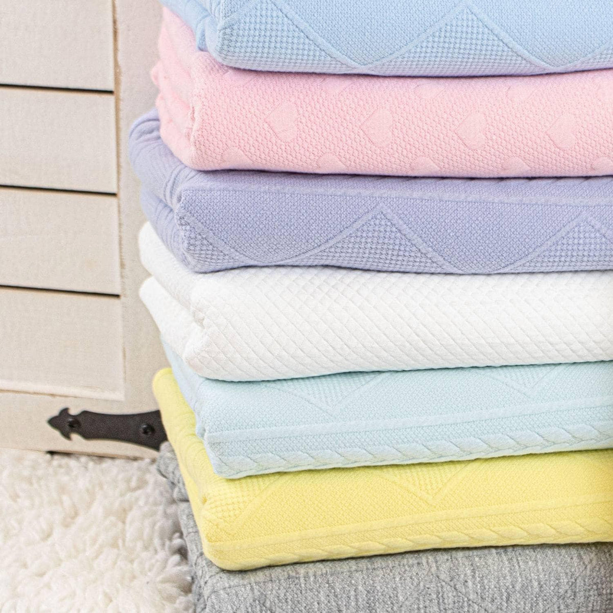 Stack of pastel knit baby blankets including a yellow knit baby blanket folded on a soft surface