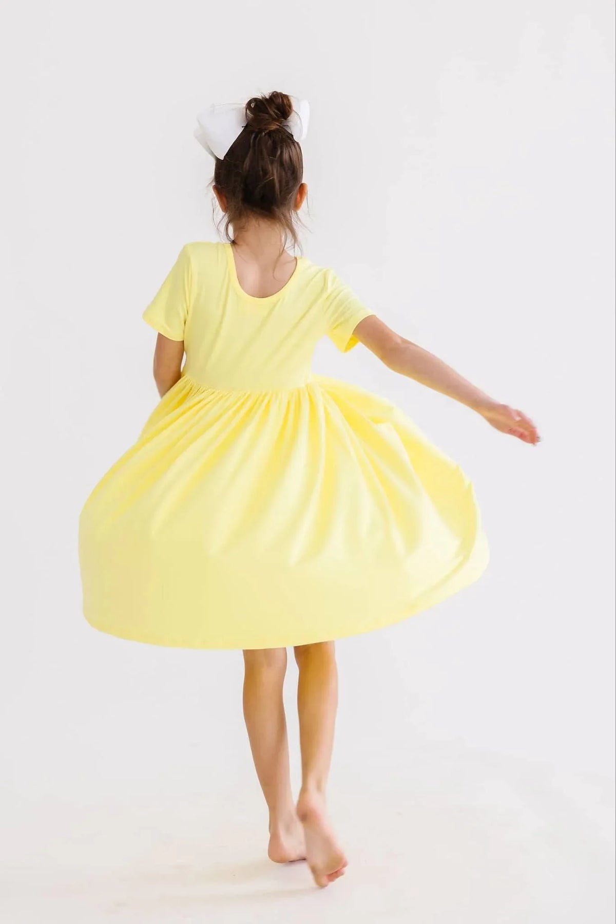 young girl wearing yellow twirl dress for girls spinning barefoot with white bow in hair
