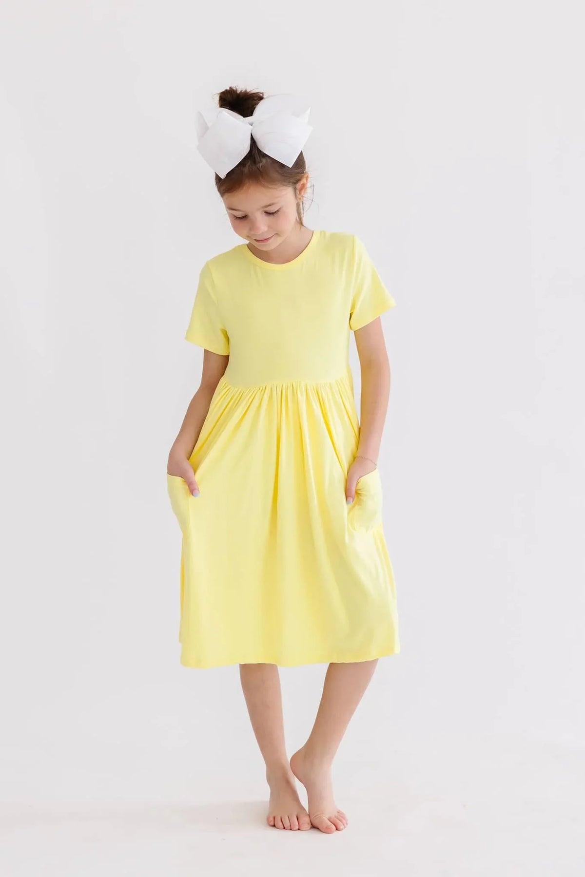 young girl wearing yellow twirl dress for girls standing barefoot with hands in pockets
