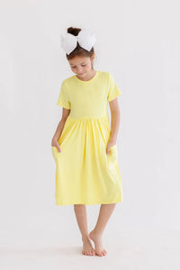 young girl wearing yellow twirl dress for girls standing barefoot with hands in pockets