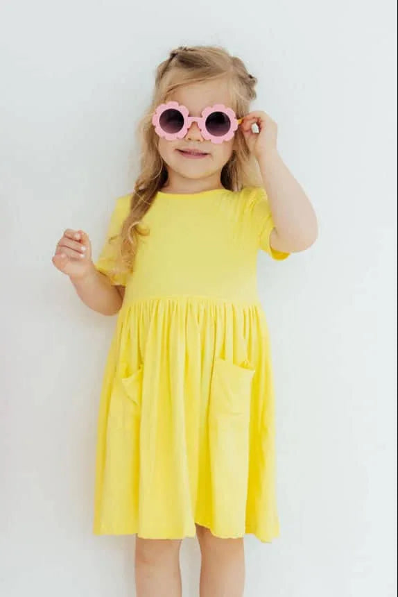 young girl wearing yellow twirl dress for girls with pockets and pink sunglasses smiling
