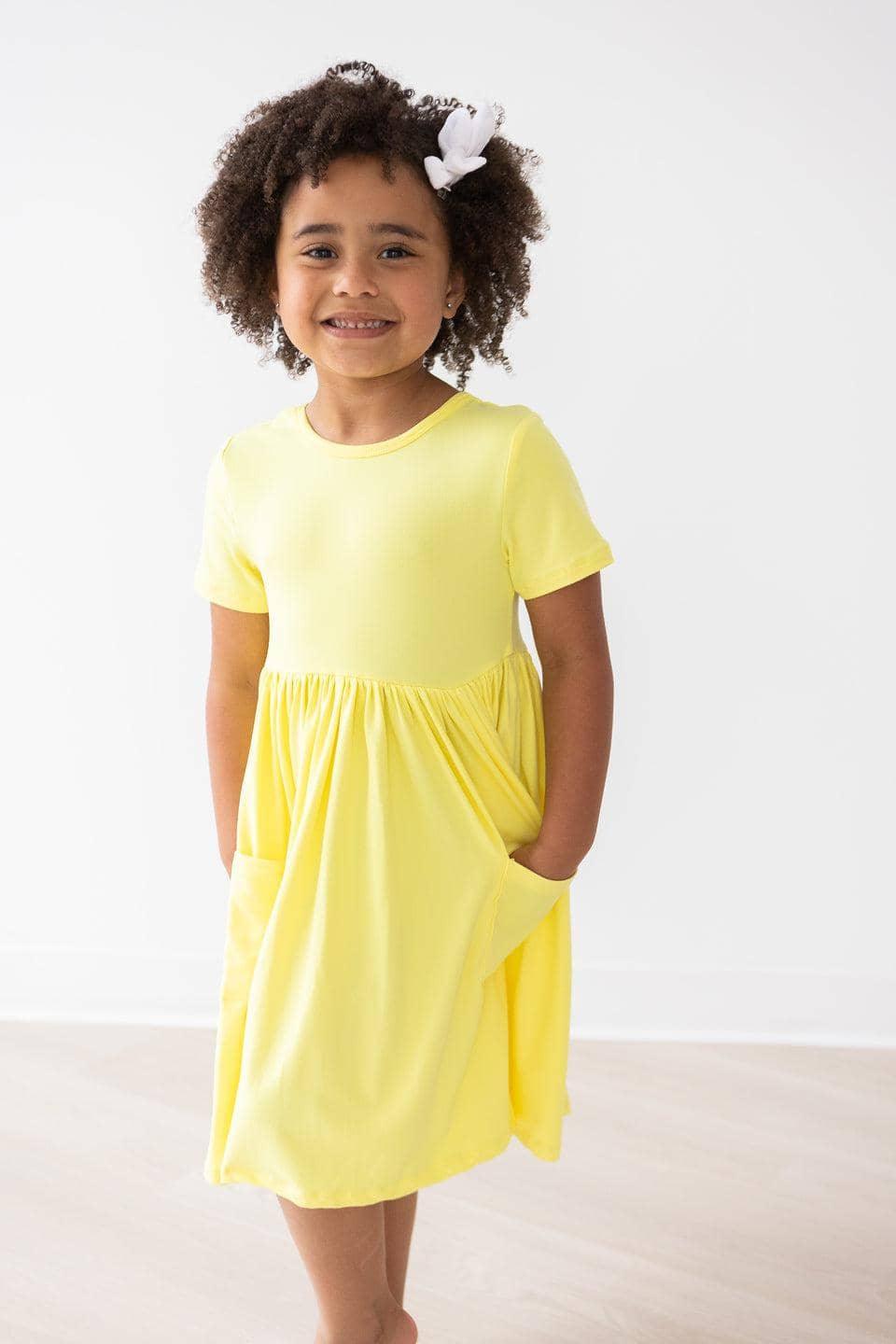 girl wearing yellow twirl dress for girls with short sleeves standing and smiling