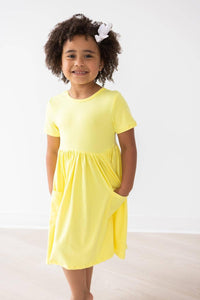 girl wearing yellow twirl dress for girls with short sleeves standing and smiling