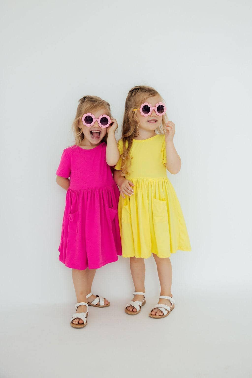 young girl wearing yellow twirl dress for girls with pockets and sunglasses smiling and posing