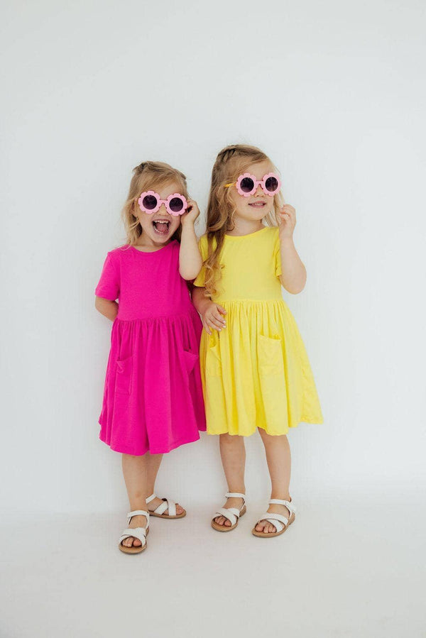 young girl wearing yellow twirl dress for girls with pockets and sunglasses smiling and posing