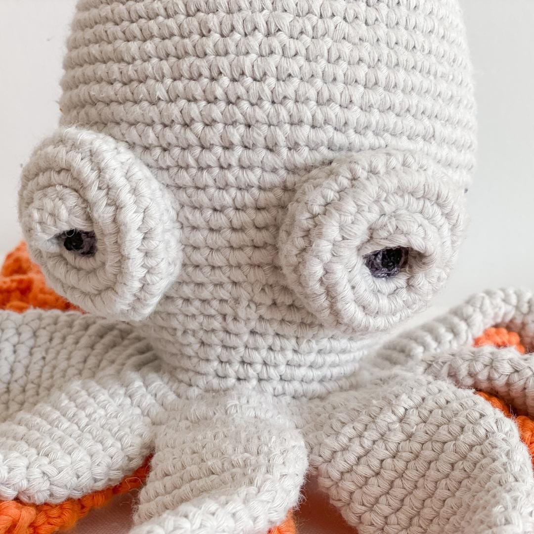 Grey crochet octopus with large embroidered eyes and bright orange underside tentacles. Soft organic cotton toy for nursery and children's rooms.