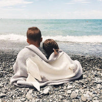 Gray and white bunny baby blanket swaddle for infants with ear and tail details sitting on pebbled beach